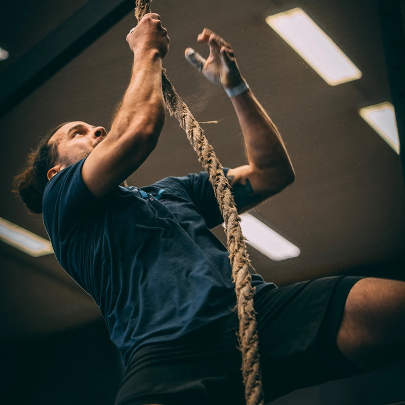 Mann klettert im Wettkampf an dickem Kletterseil in der Cross Equip Trainingshalle
