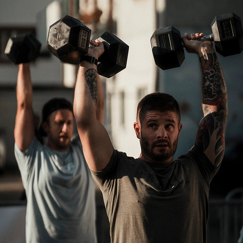 Zwei Männern heben die Hex Dumbbells von cross equip nach oben und sind draußen