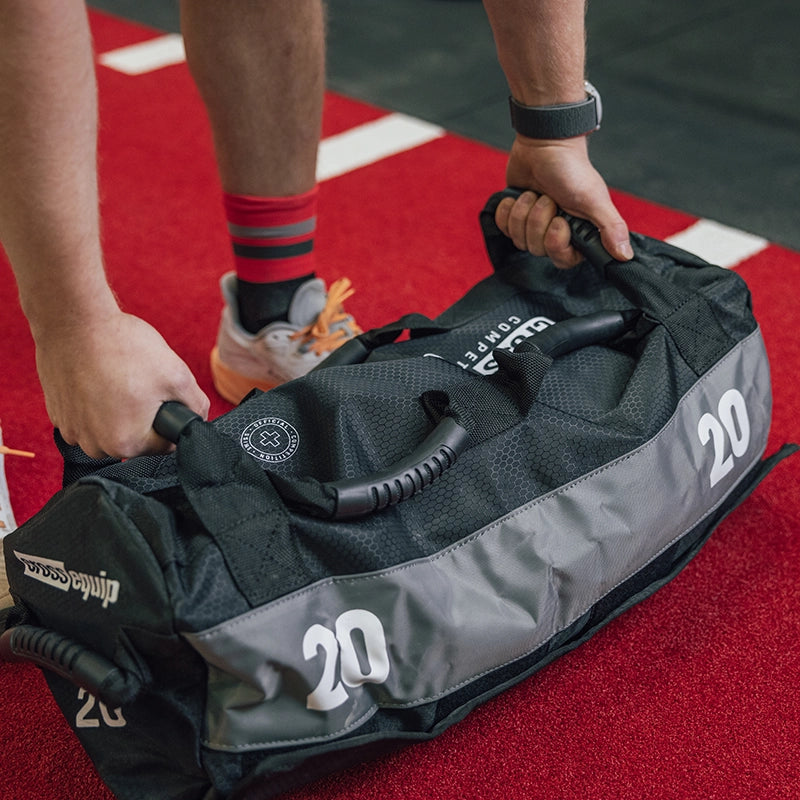 Cross Equip Competition Sandbag 20kg wird mit beiden Griffen vom Boden gehoben