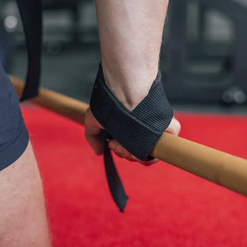 Schwarze Lifting Straps beim Deadlift – Hand greift goldene Langhantelstange im Gym