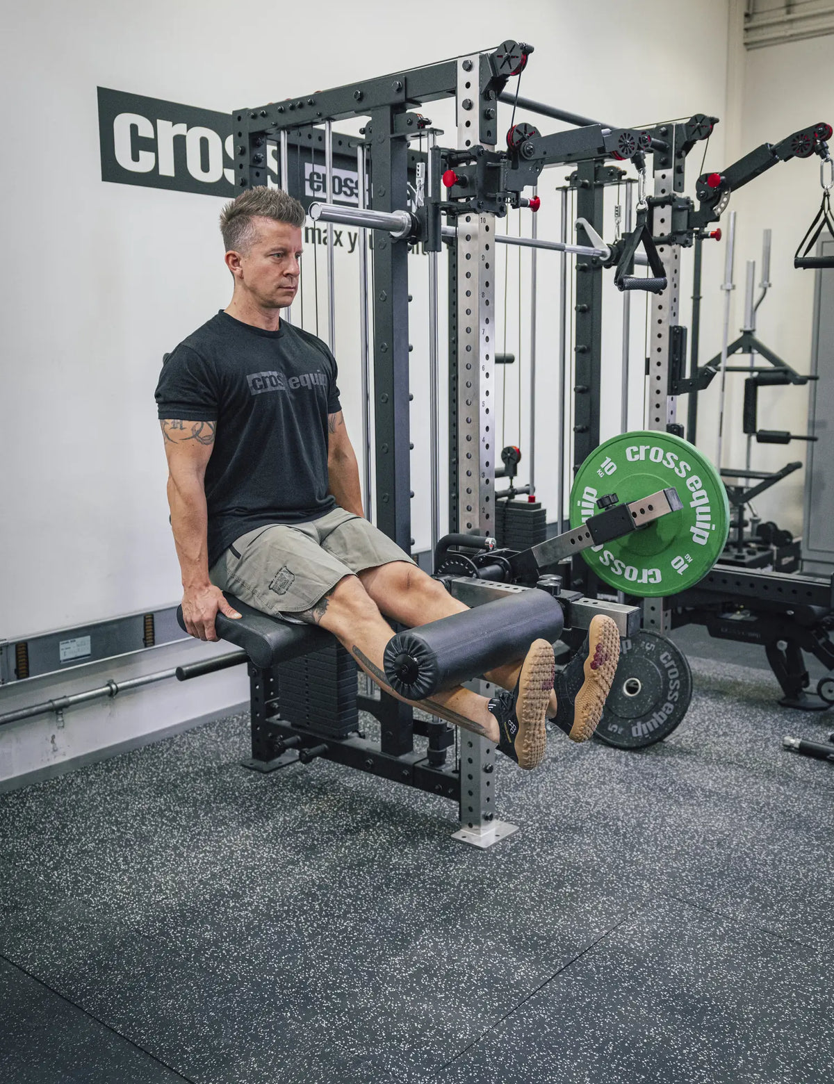 Leg Extension sitzend auf dem Armpolster des Attachments – die Schienbeine drücken die Schaumstoffrolle nach oben, beladen mit einer Bumper Plate