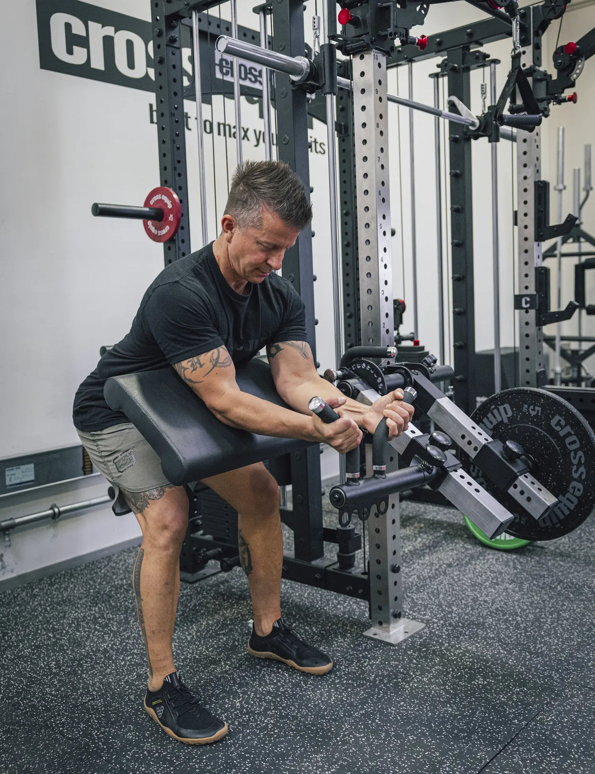 Preacher Curl am Leg Extension & Curl Attachment – die Oberarme liegen auf dem Armpolster, die Hände an den abgewinkelten Griffen, am Rack montiert