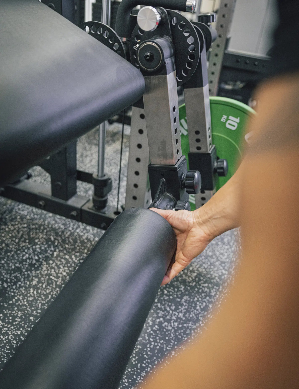 Eine Hand verschiebt die Schaumstoffrolle am Leg Extension & Curl Attachment entlang der gelochten Hülse