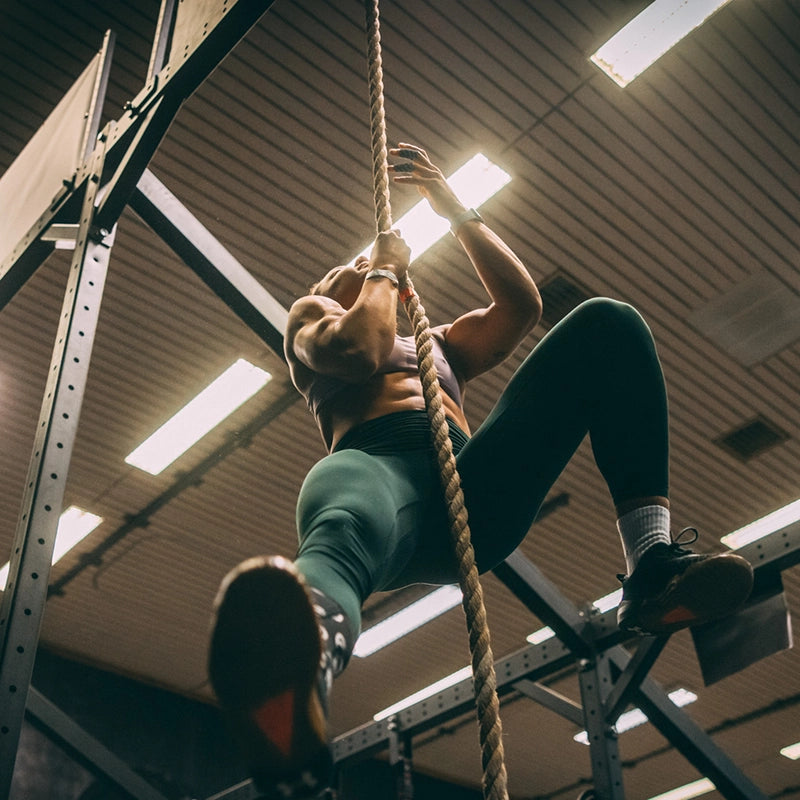 Athletin klettert am Kletterseil vor Rack im Cross Equip Gym