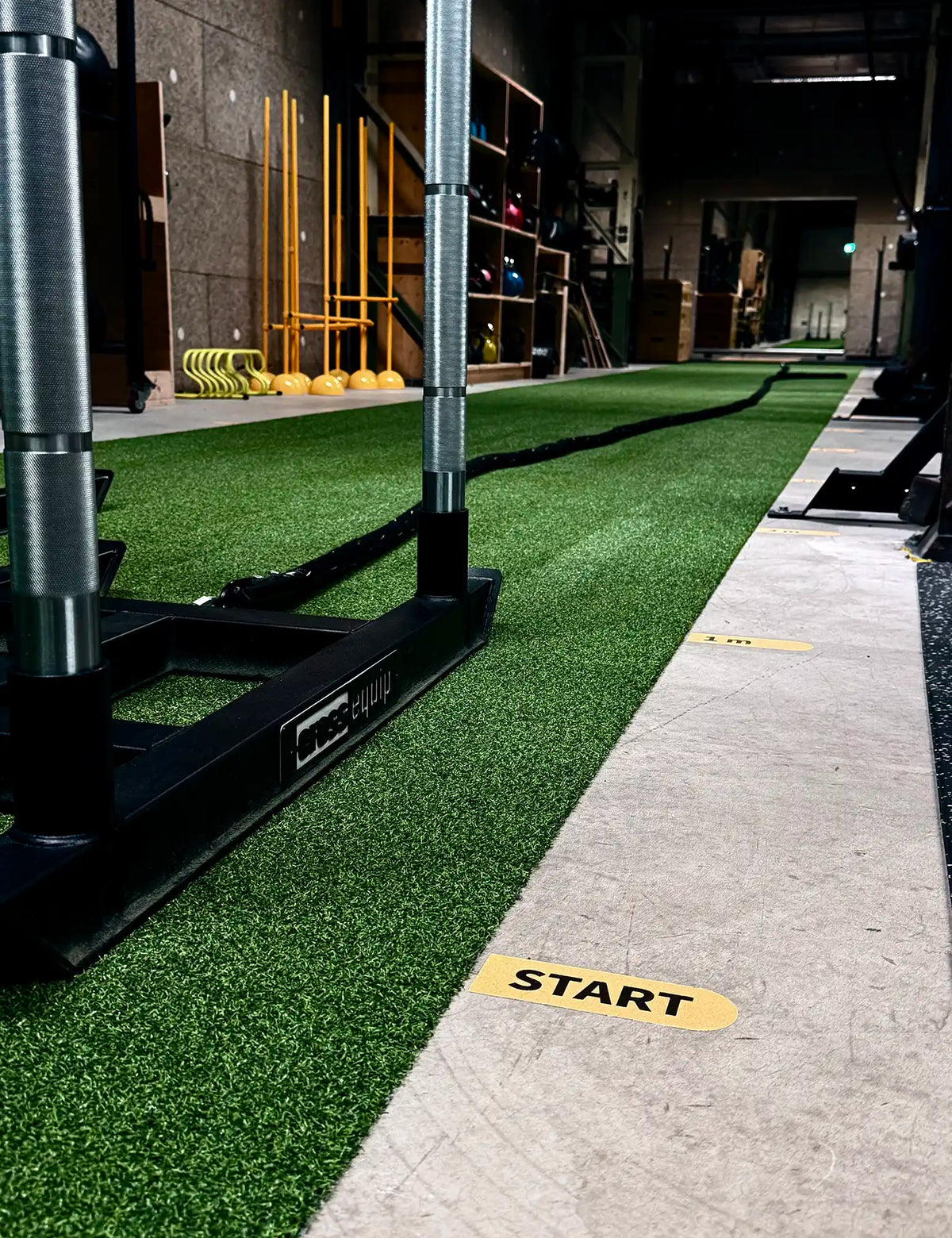 Eco Turf in Grün als Sprintbahn im Gym – Schlitten von cross equip auf der Bahn, daneben Betonboden mit gelber START-Markierung