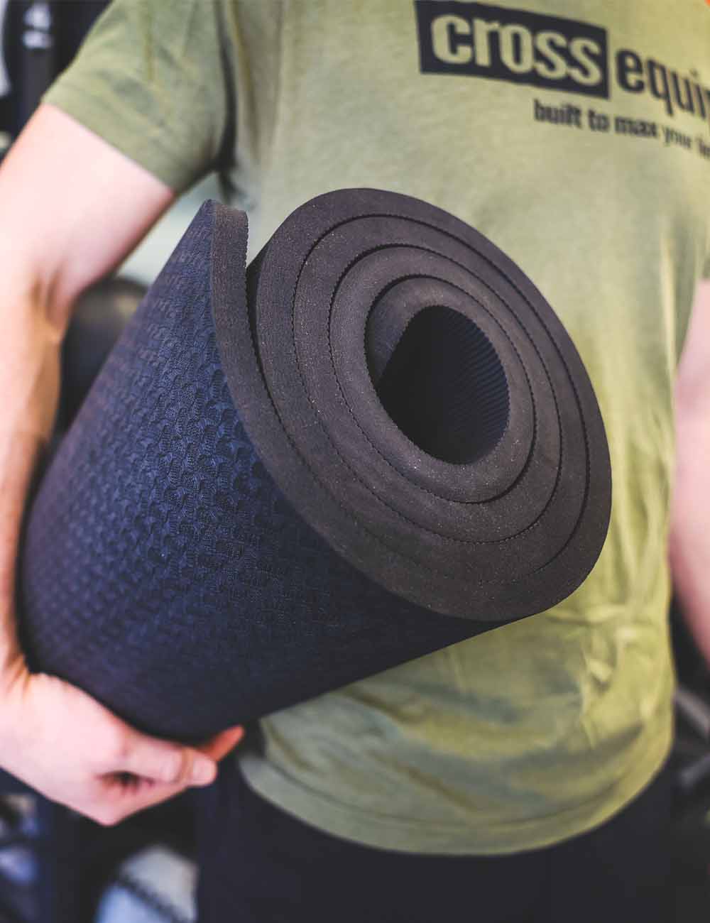 Aufgerollte schwarze TPE Yoga Matte unter dem Arm getragen – die Rolle zeigt die dicke Materiallage im Querschnitt