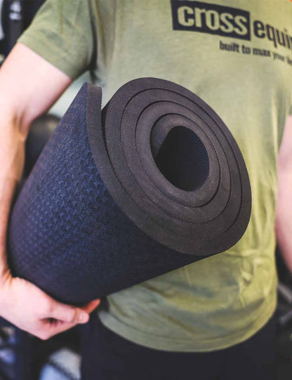 Aufgerollte schwarze TPE Yoga Matte unter dem Arm getragen – die Rolle zeigt die dicke Materiallage im Querschnitt